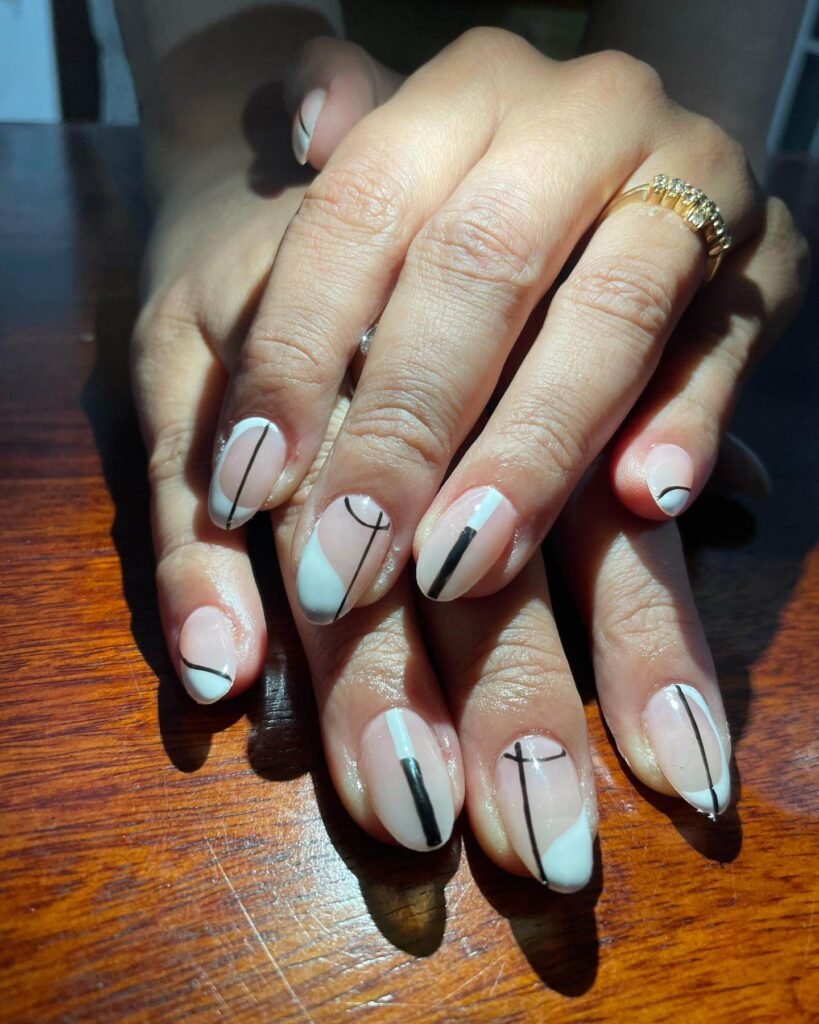 Almond-shaped nails with crisp black triangles and gold accents on a matte white background by nailmasterindia07
