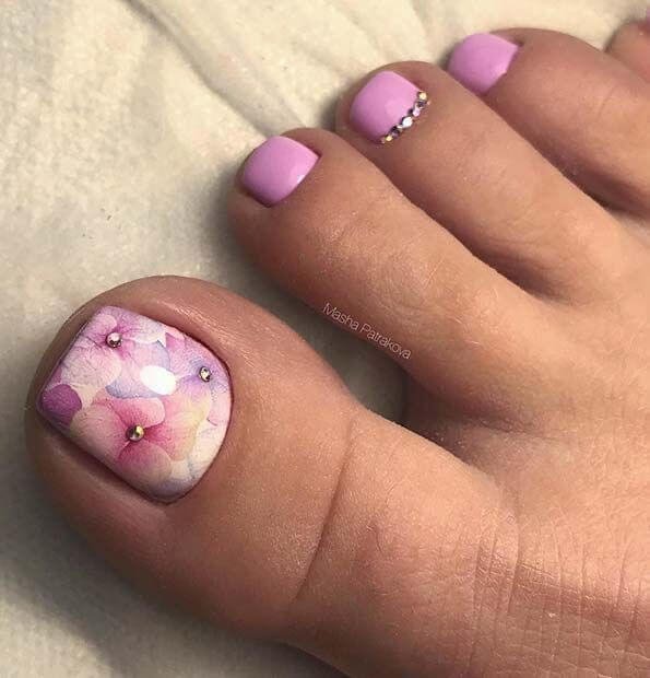 Soft artistic shot of watercolor flower toe nails styled with real flowers and watercolor paints. by nailbeautyguide