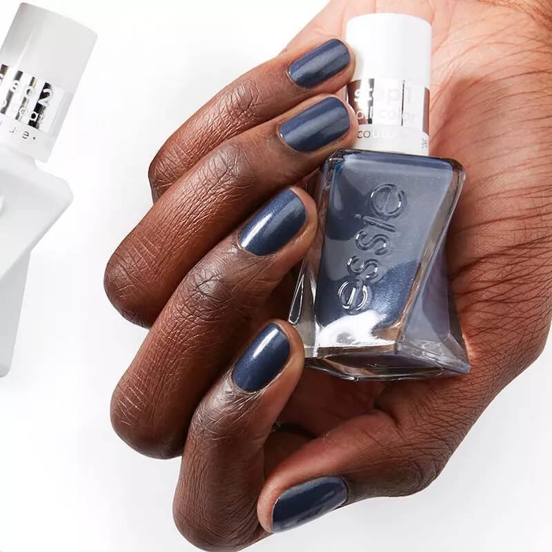 Nails painted in a deep, moody blue color that has a hint of grey by essie