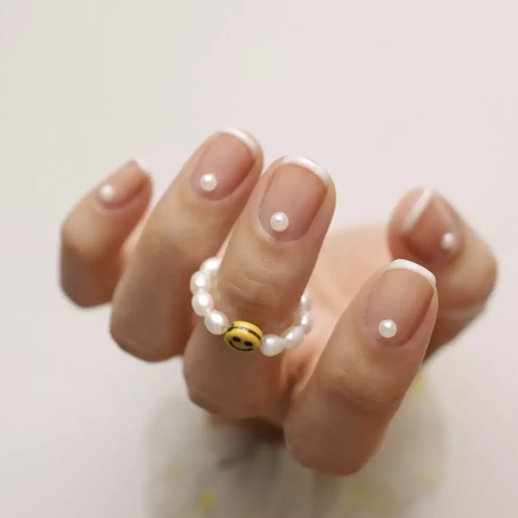 Image of a classic white French manicure with a single pearl placed at the base of each nail by thehangedit