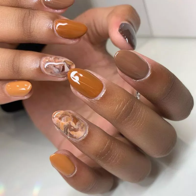 Image of nails alternating between solid neutral brown colors and one statement nail with a marbled caramel detail. by bysadiedaisy