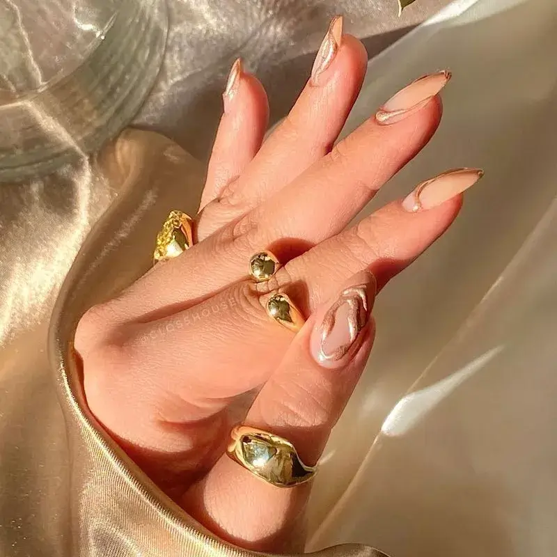 Image of nails with a subtle, shimmering champagne base featuring abstract rose gold swirls. by glosshouse