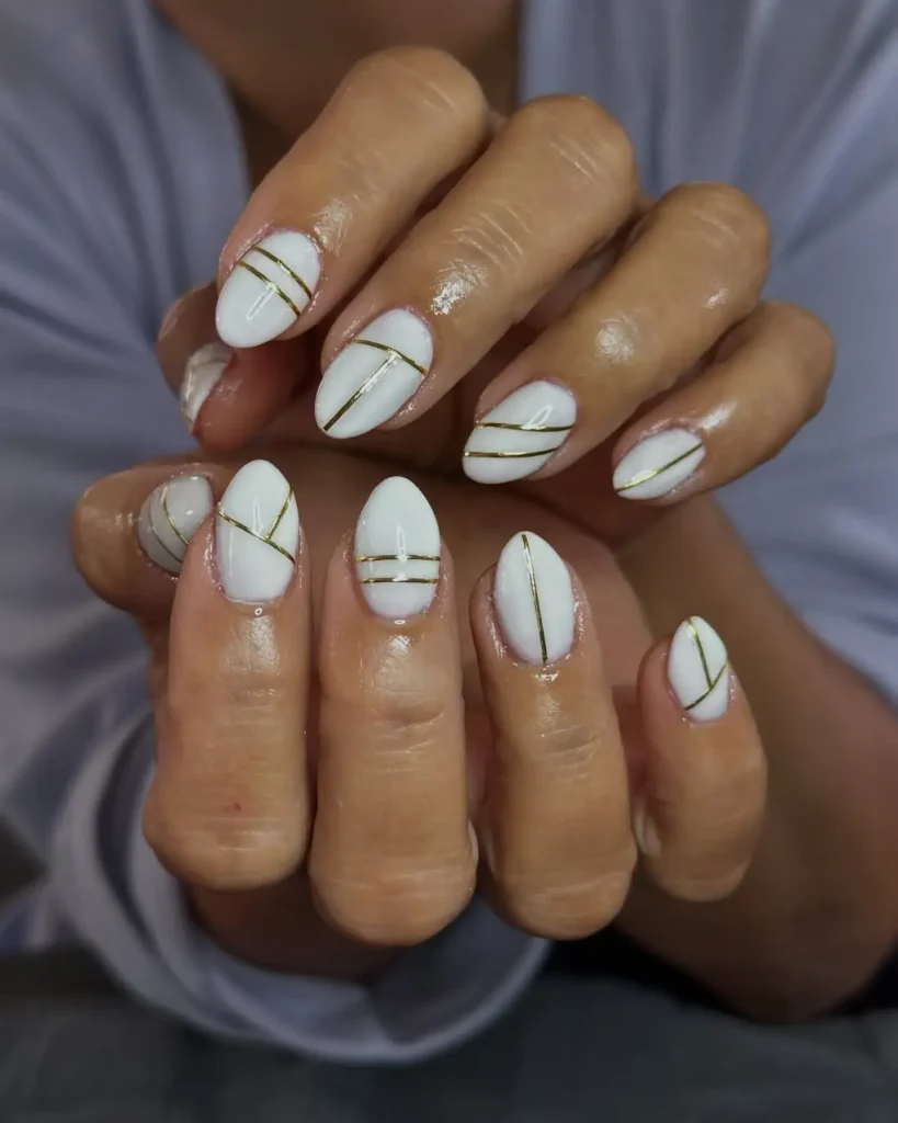 Image of square-tipped nails painted white with thin, horizontal gold lines painted across the tips. by brushednailsalon
