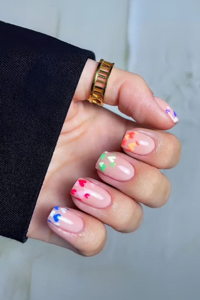 Nude nails with colorful heart accents in red, pink, blue, and green. by nails.by.iz