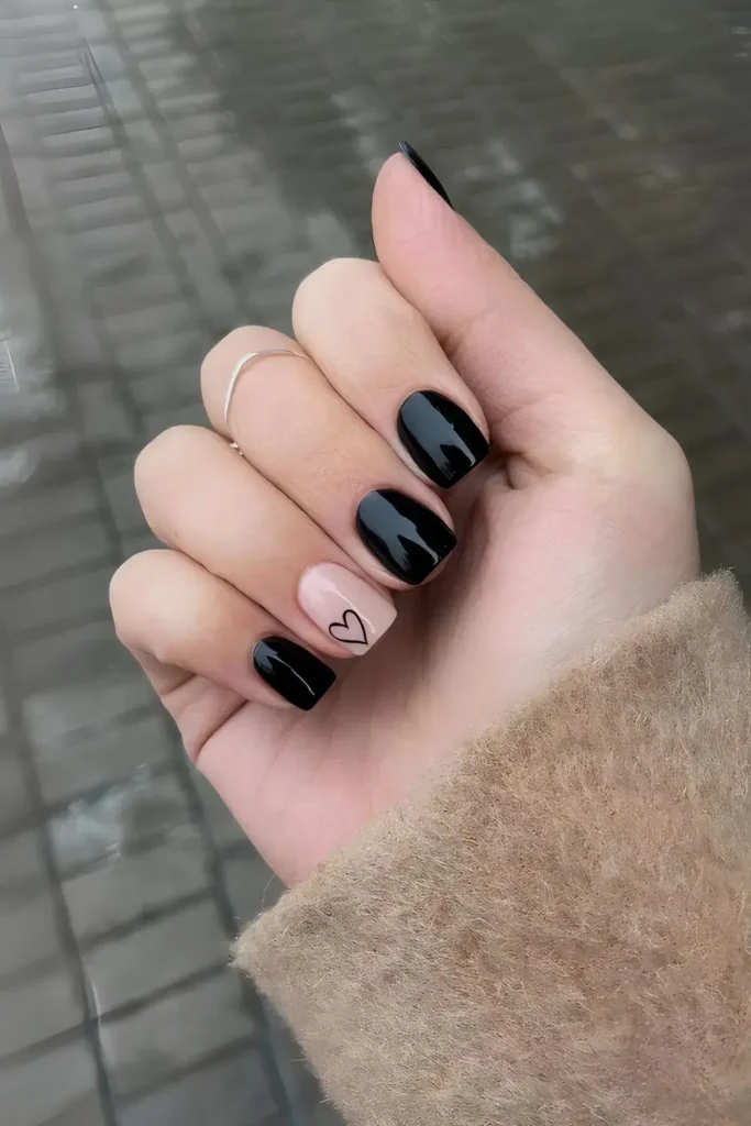 Solid black nails with an outlined heart accent on one nail. by nailbeautyguide