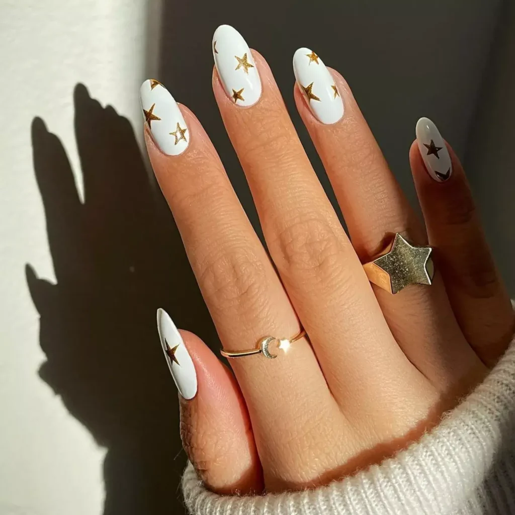 White oval nails adorned with tiny gold star accents. by amyle.nails